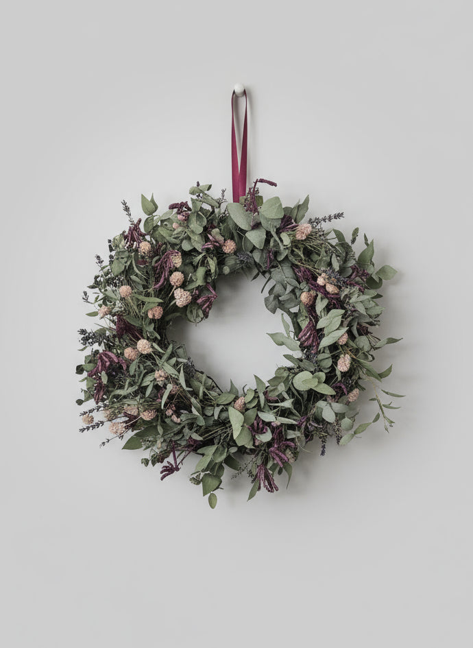 Dried flowers and eucalyptus Christmas wreath with a crimson ribbon on a plain background