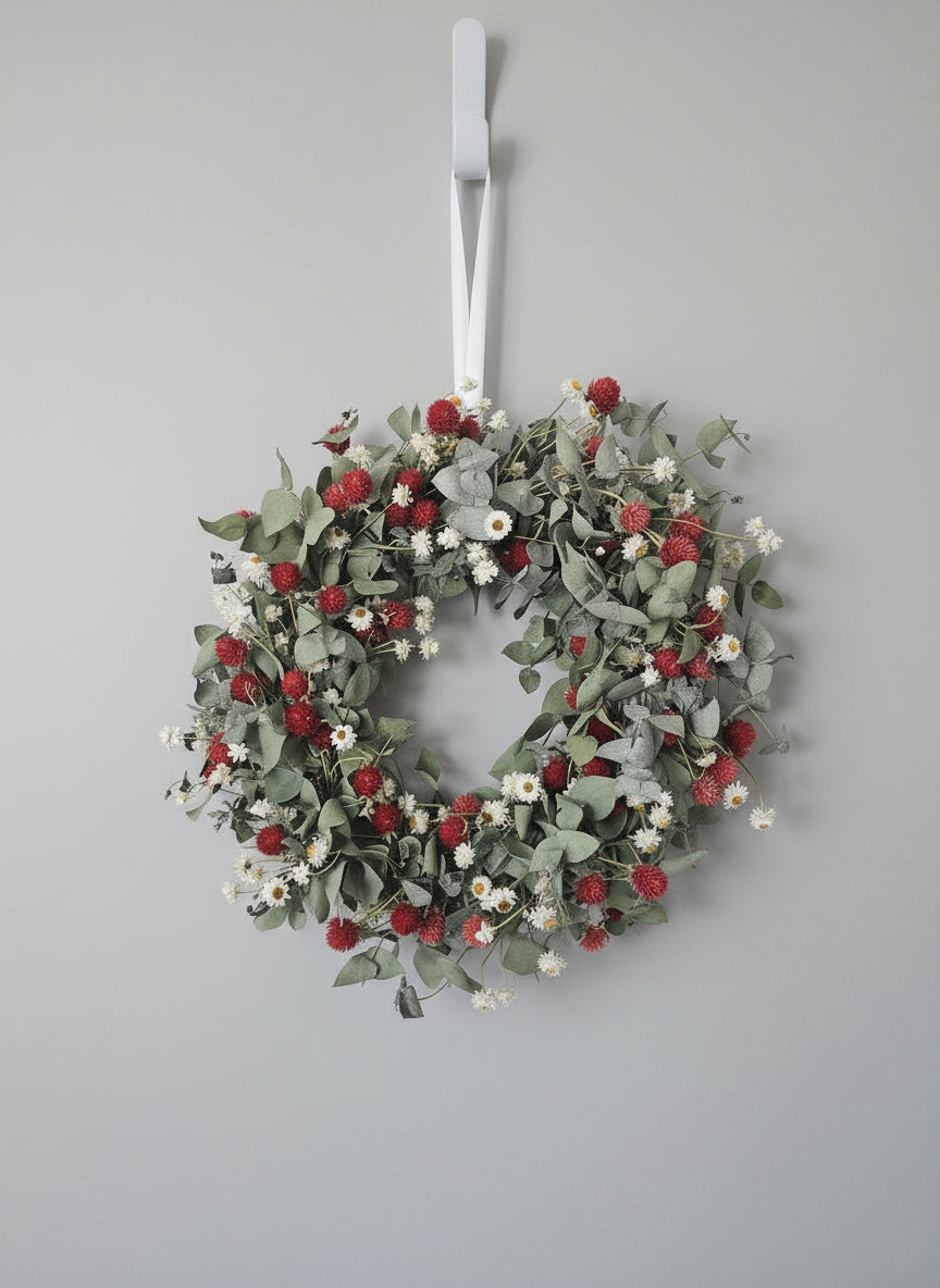 Decorative wreath with red berries and green leaves hanging on a white door.