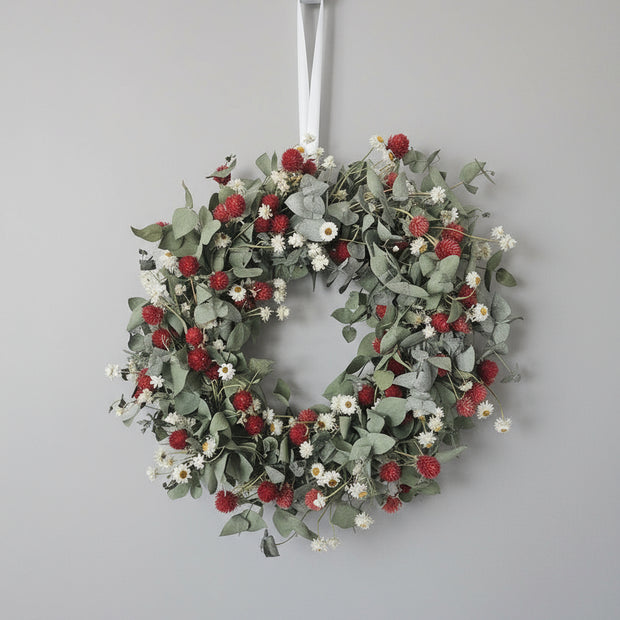 Decorative wreath with red berries and green leaves hanging on a white door.