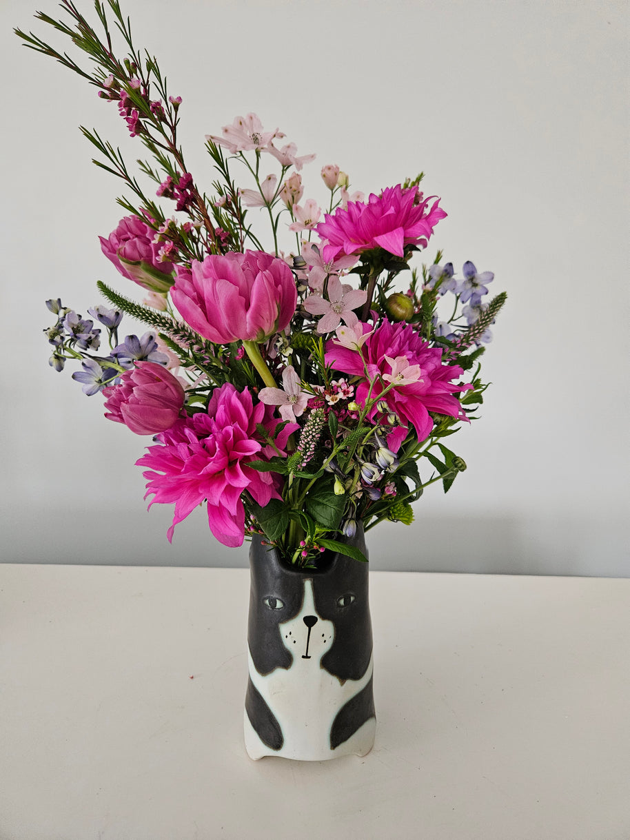 Bouquet of pink and purple flowers in a black and white vase designed like a dog's face on a white background