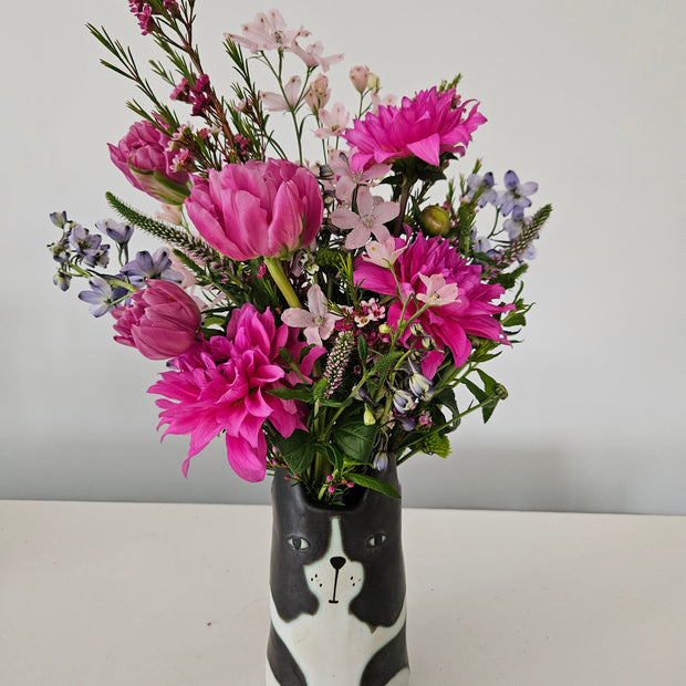 Bouquet of pink and purple flowers in a black and white vase designed like a dog's face on a white background