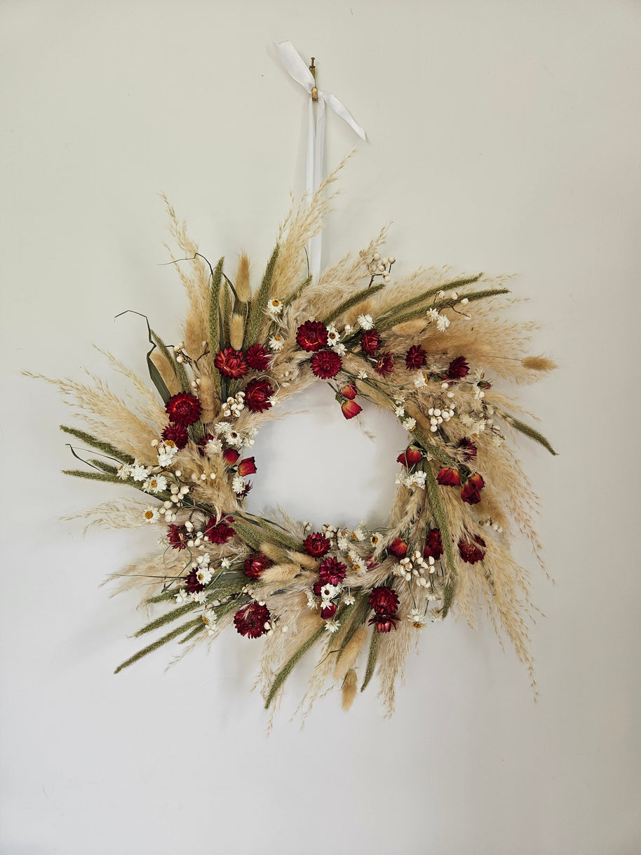 Decorative wreath with red flowers and dried grasses on a white wall
