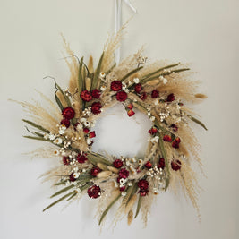 Decorative wreath with red flowers and dried grasses on a white wall
