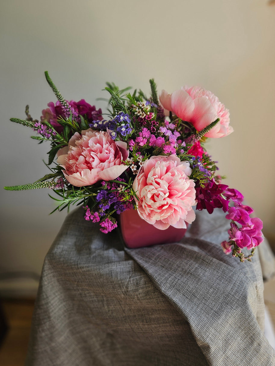 Pink and purple flowers in a pot on a grey tablecloth