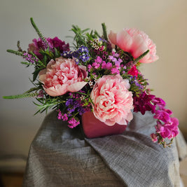 Pink and purple flowers in a pot on a grey tablecloth