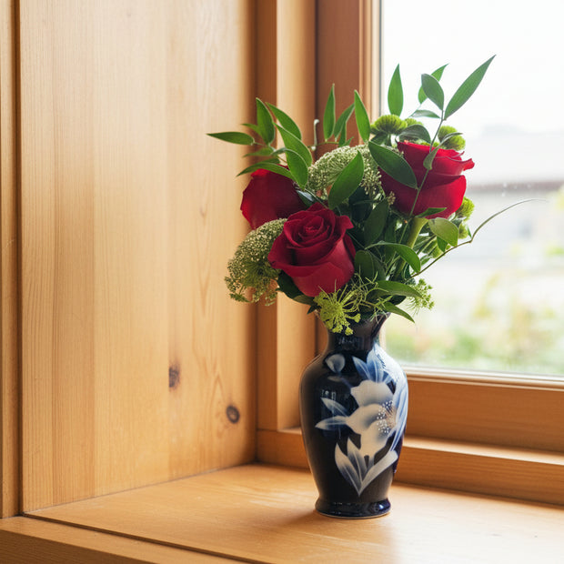 Bouquet of red roses and greenery in a decorative vase on a plain background