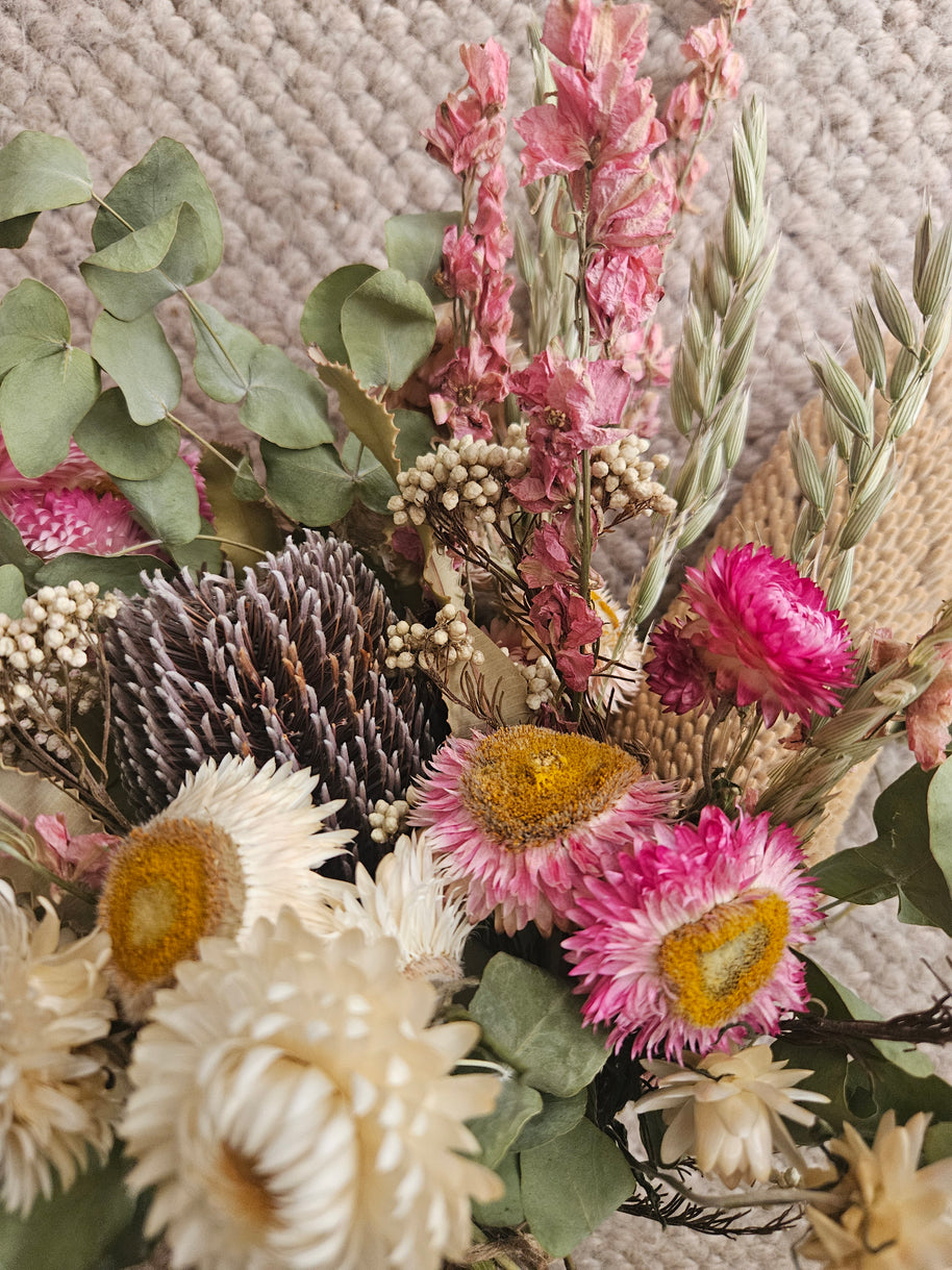 Close-up of a bouquet of dried flowers with pink, green, and brown colors on a textured surface.