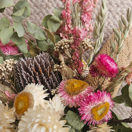 Close-up of a bouquet of dried flowers with pink, green, and brown colors on a textured surface.