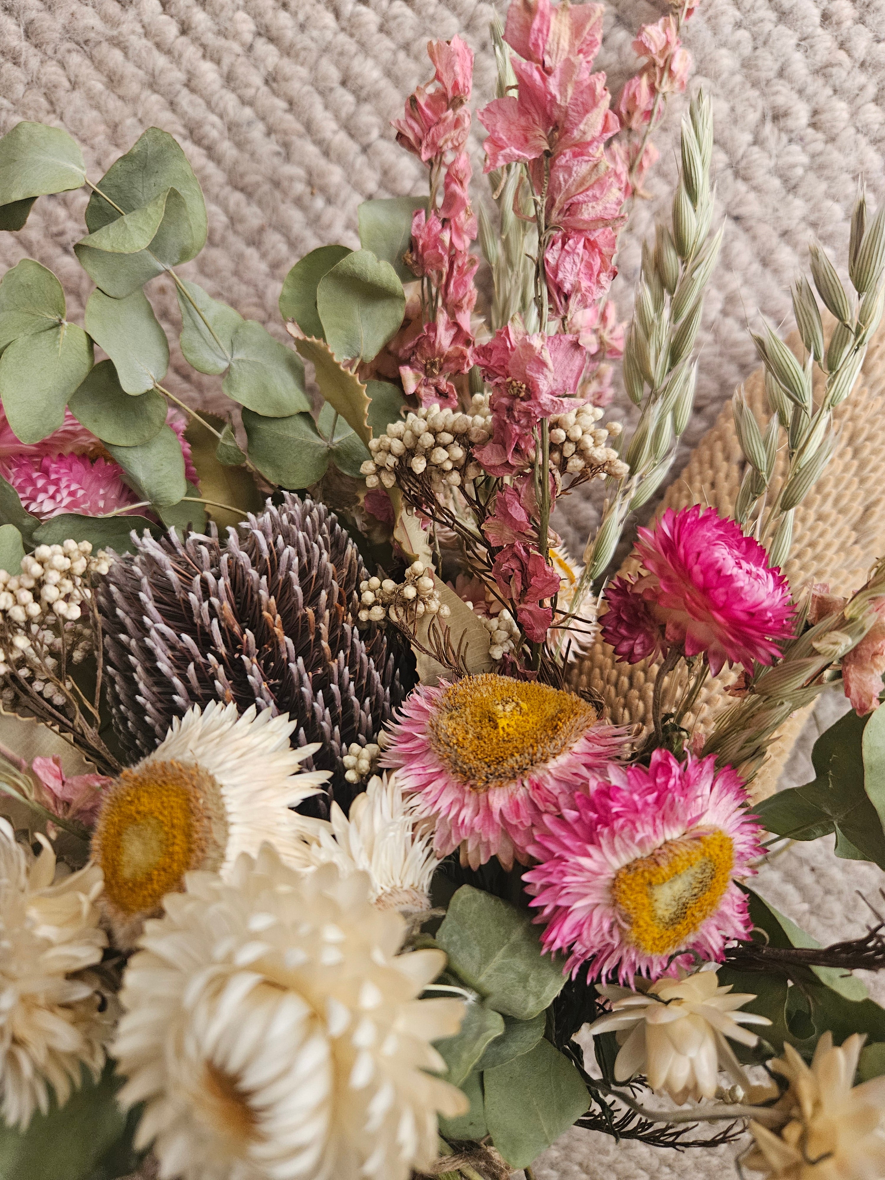 Close-up of a bouquet of dried flowers with pink, green, and brown colors on a textured surface.