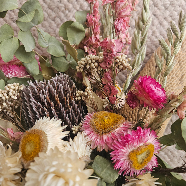 Close-up of a bouquet of dried flowers with pink, green, and brown colors on a textured surface.