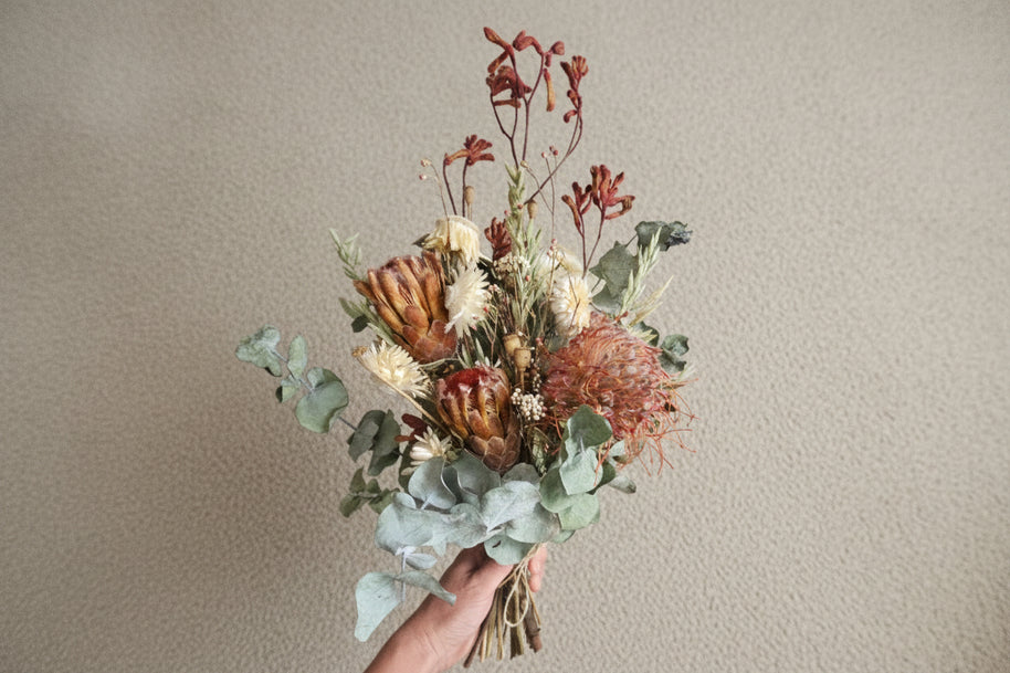 Bouquet of dried flowers held by a person on a carpeted floor.