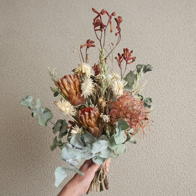 Bouquet of dried flowers held by a person on a carpeted floor.