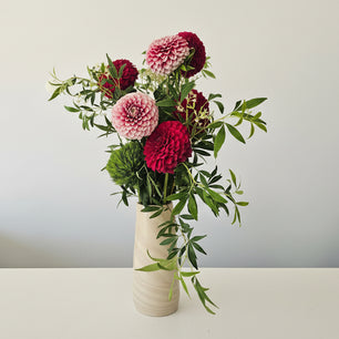 Floral arrangement with red and white flowers in a white vase against a light grey background