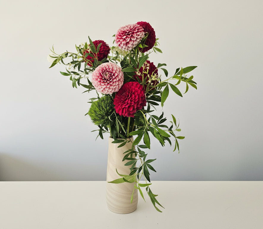 Floral arrangement with red and white flowers in a white vase against a light grey background
