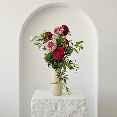 Floral arrangement with red and white flowers in a white vase against a light grey background