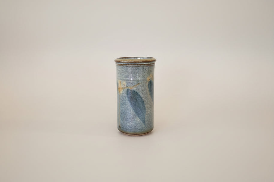 Cylindrical ceramic vase with blue leaves on a white background