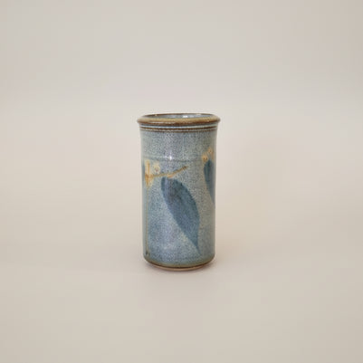 Cylindrical ceramic vase with blue leaves on a white background