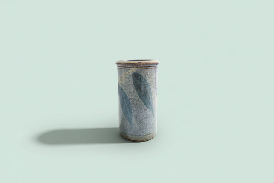 Cylindrical ceramic vase with blue and gray glaze on a green background