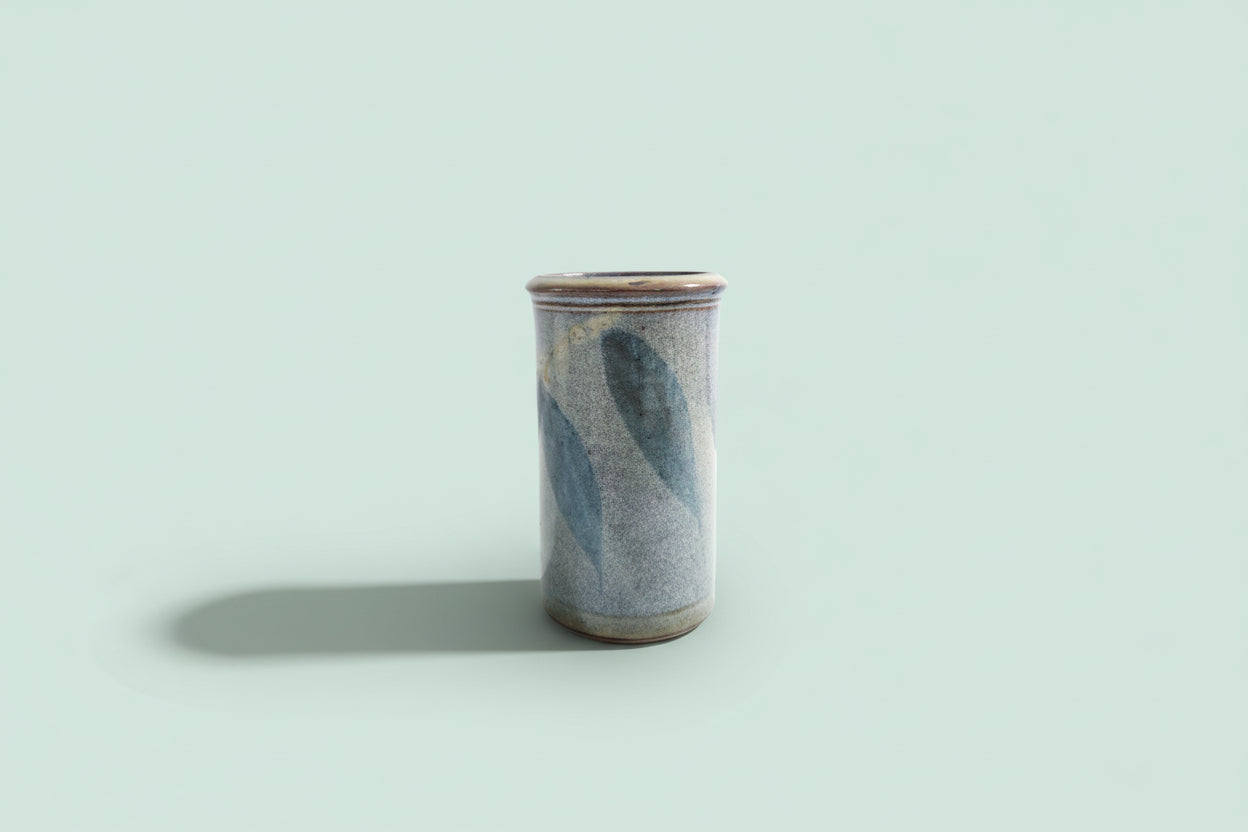 Cylindrical ceramic vase with blue and gray glaze on a green background