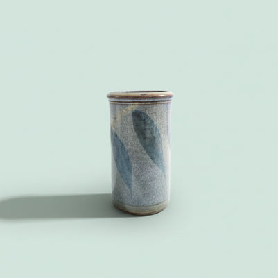 Cylindrical ceramic vase with blue and gray glaze on a green background