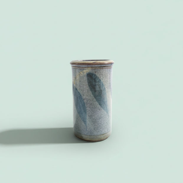 Cylindrical ceramic vase with blue and gray glaze on a green background