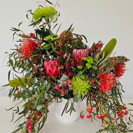 Green and red flower arrangement in a white pot