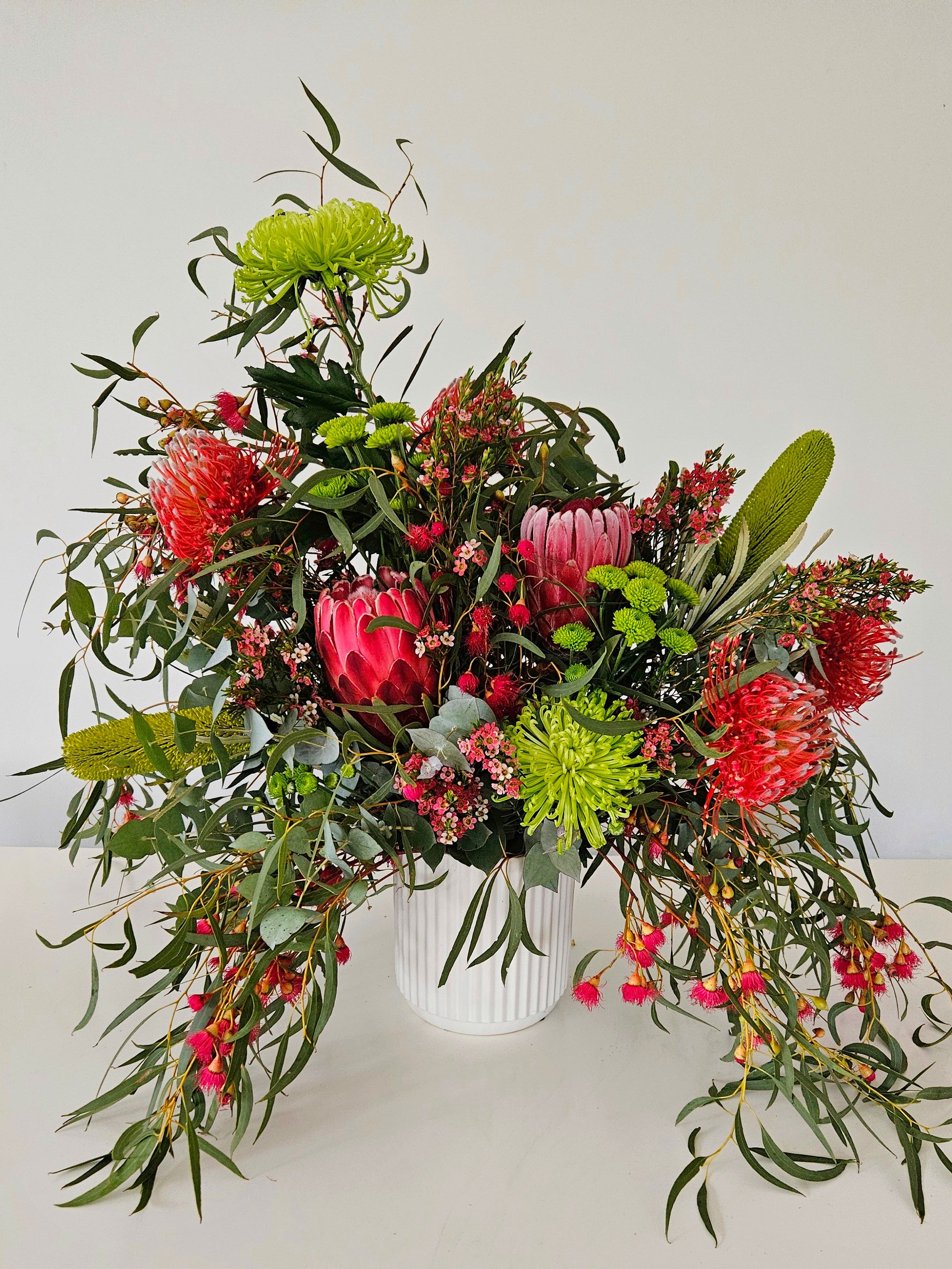 Green and red flower arrangement in a white pot