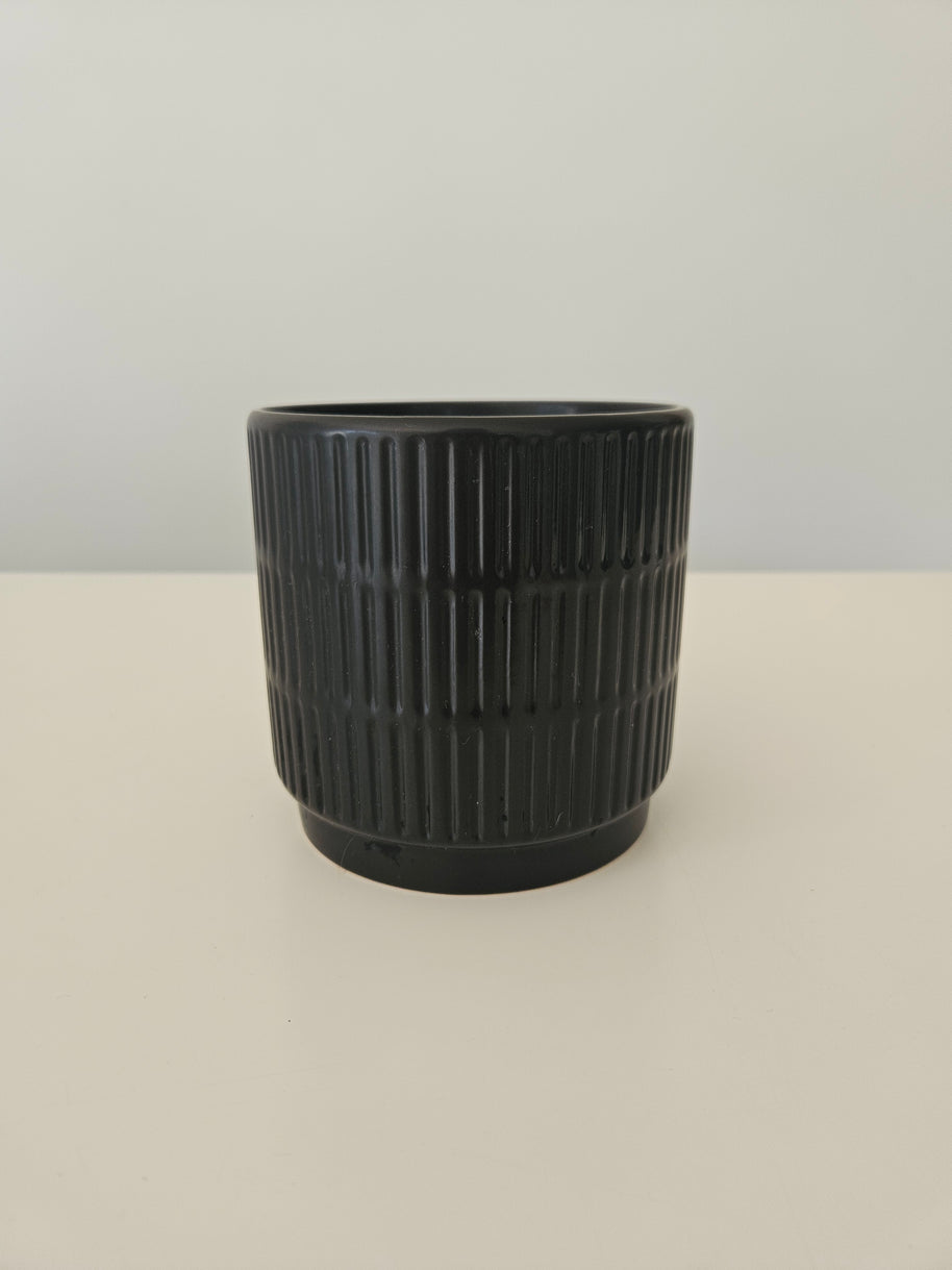 Side view of a black pot with a vertical pattern on a white background