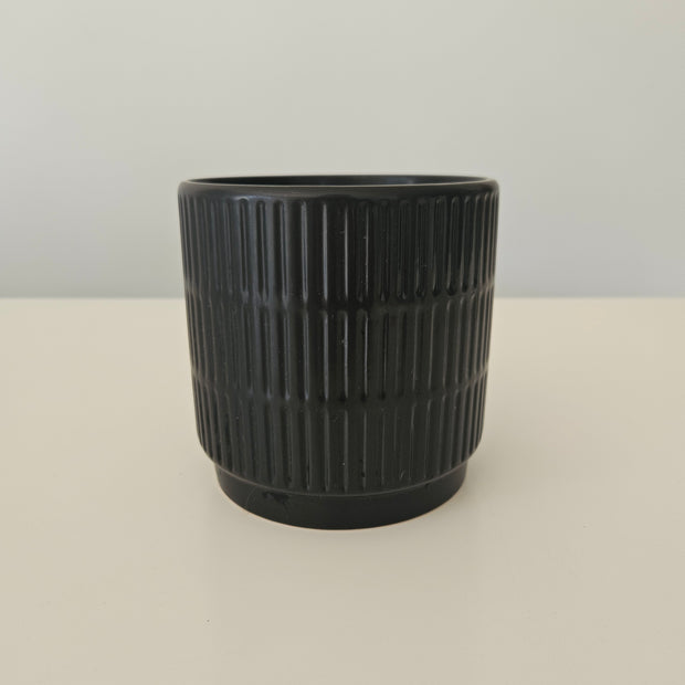 Side view of a black pot with a vertical pattern on a white background