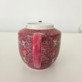 Decorative red and pink ceramic teapot with intricate patterns on a white background