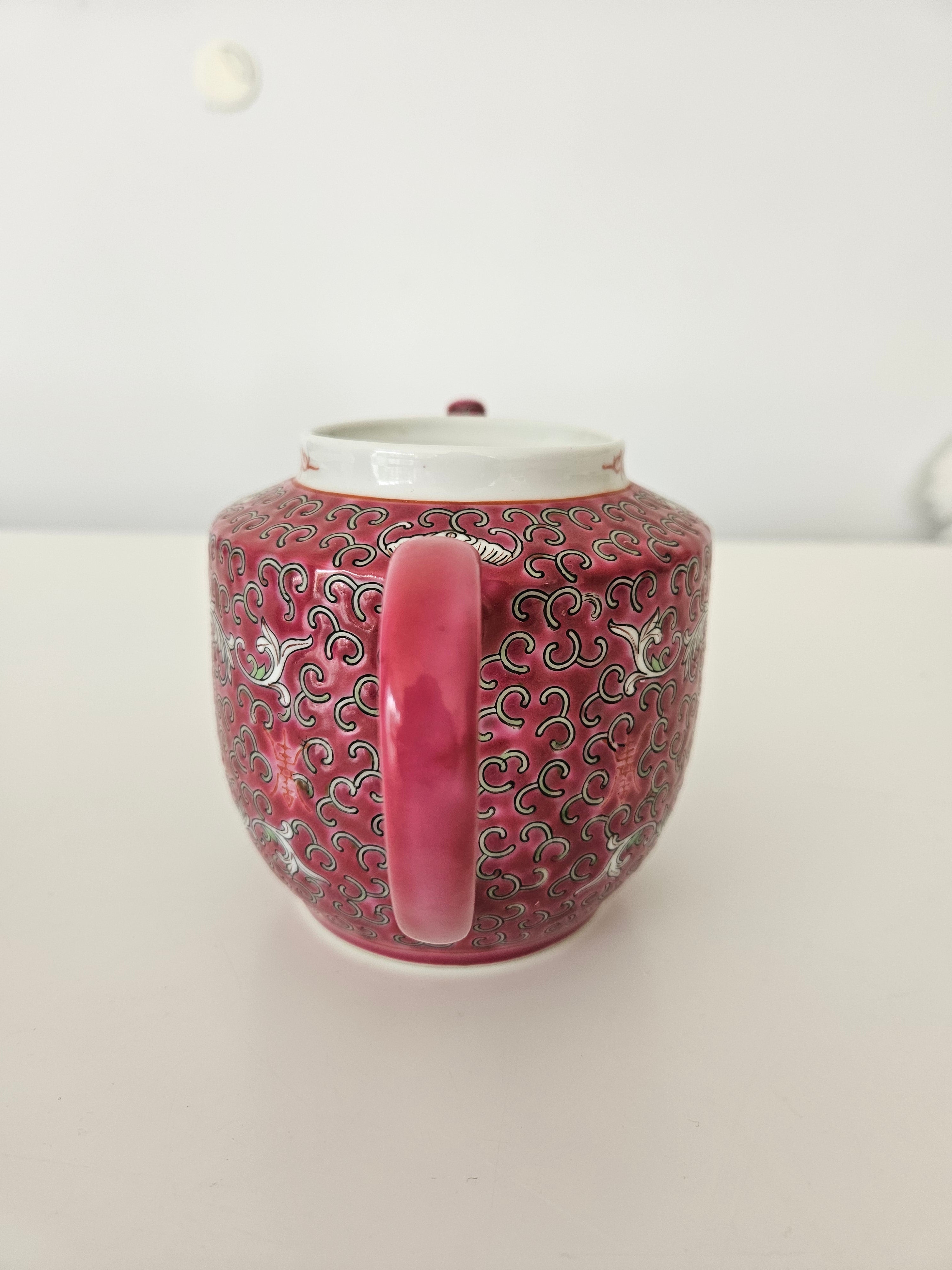 Decorative red and pink ceramic teapot with intricate patterns on a white background