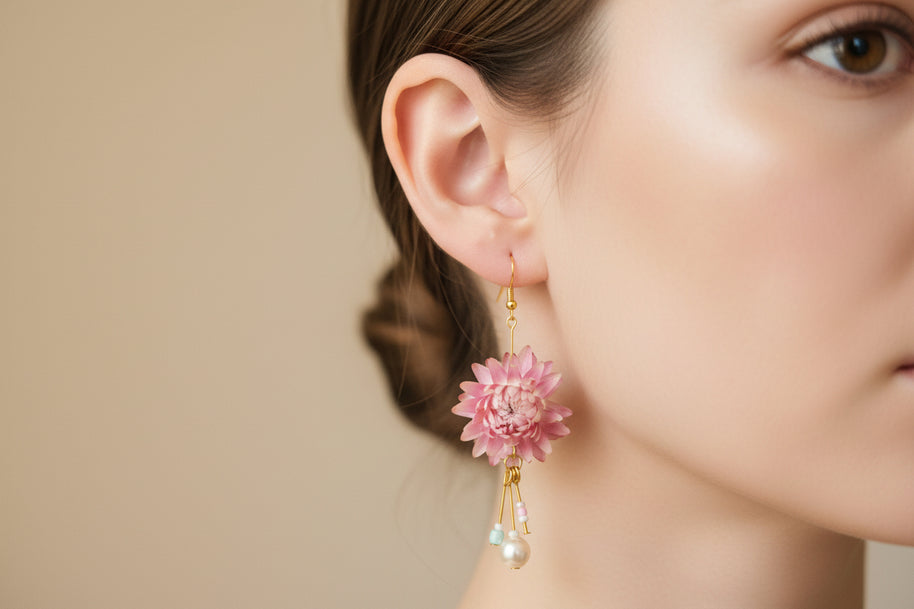 Pink floral earrings with gold and pearl accents on a black card against a light grey background