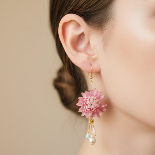 Pink floral earrings with gold and pearl accents on a black card against a light grey background