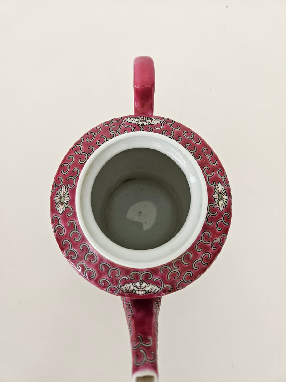 Ceramic red teapot with decorative pattern and handle on a light background