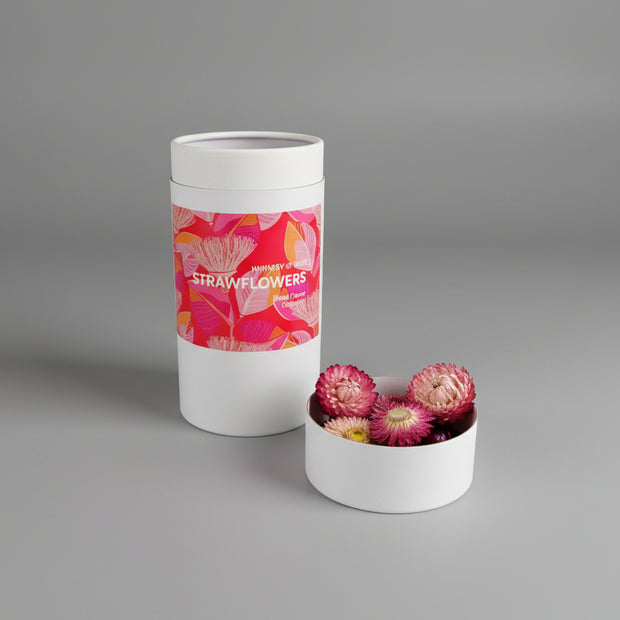 Container of strawflowers with a pink label on a white surface